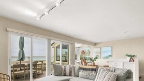 Un vaste salon doté d’une grande porte-fenêtre coulissante donnant sur un balcon, d’un canapé agrémenté de coussins à motifs et d’un coin repas avec des meubles en bois.