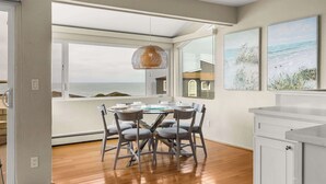 Un espace repas comprenant une table et des chaises, un luminaire suspendu et une vue sur l’océan grâce à de grandes fenêtres.