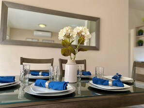 A dining table set with white plates, blue napkins, and a vase with white flowers. - Sister Houses in private gated community with pool 5 min Airport and Consulate (Hermosillo)