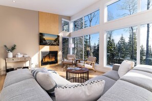 A modern living room with a fireplace, large windows, and a cozy seating area. - Hôtel à la maison - Le Capri Charlevoix, spa et nature (Les Ã�Boulements)