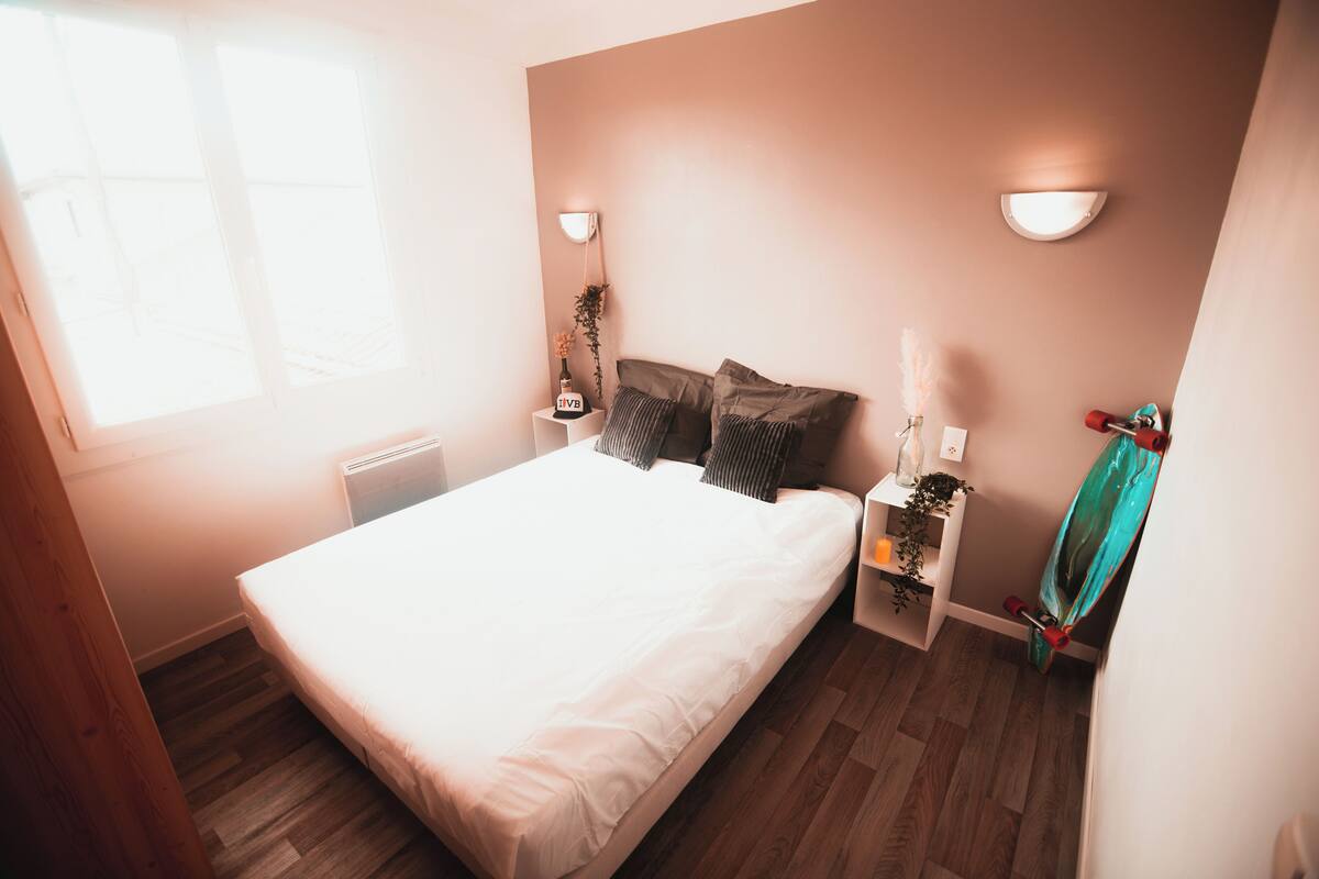 Ein Schlafzimmer mit Bett, Nachttischen, einer Wandlampe, einem Heizkörper und einem Fenster.