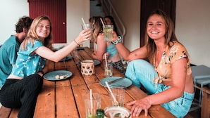 A group of people sitting around a wooden table with drinks, plates, and cutlery. - Surfbase Vieux Boucau (Vieux-Boucau-les-Bains)