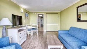 Ein Zimmer mit einem blauen Sofa, einem weißen Schminktisch, einem Schreibtisch mit Stühlen und einem großen Spiegel an der Wand.