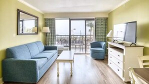 Ein Zimmer mit einer Couch, einem Sessel, einem Fernseher und einem Balkon mit Blick.