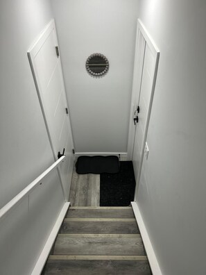 A staircase with a black mat at the bottom, white walls, and a circular object on the wall. - Private 1-BR Suite | Full Kitchen, Free Parking, Laundry - SW Edmonton (Edmonton)