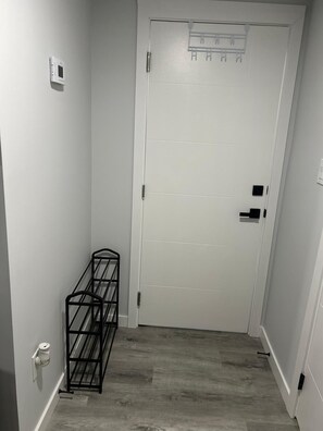 A narrow hallway with a white door, a metal rack, and a small trash bin. - Private 1-BR Suite | Full Kitchen, Free Parking, Laundry - SW Edmonton (Edmonton)