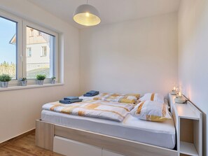A bedroom with a bed, bedside table, lamp, window, and potted plants.