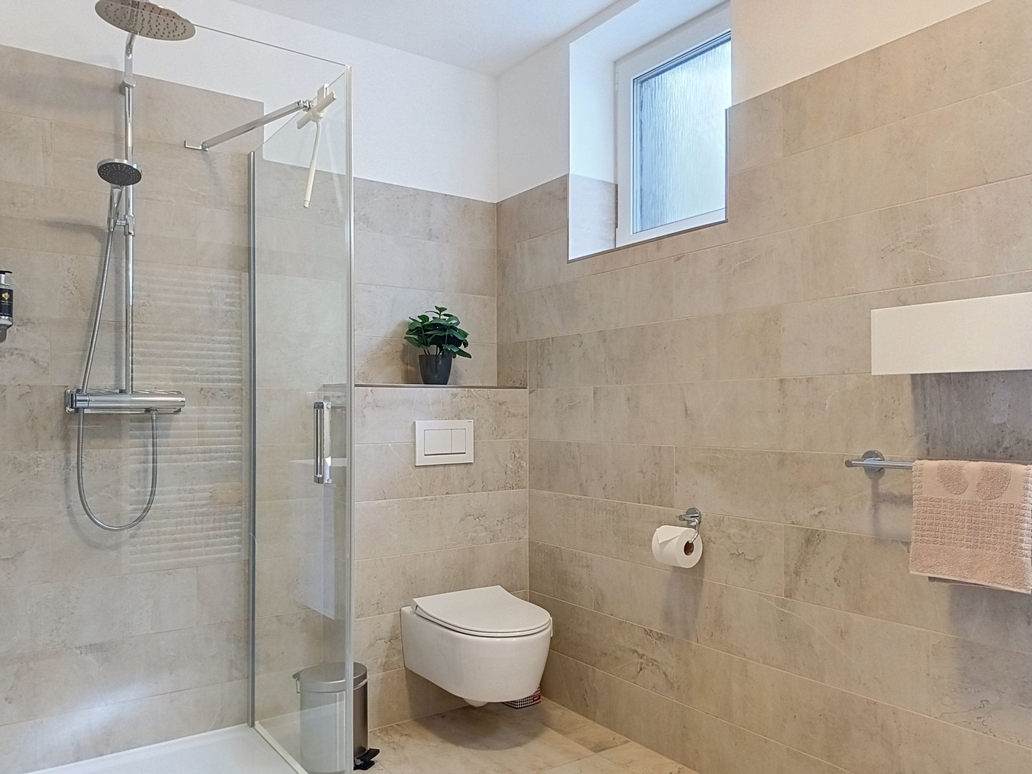 A modern bathroom with a glass-enclosed shower, a toilet, and a towel rack.