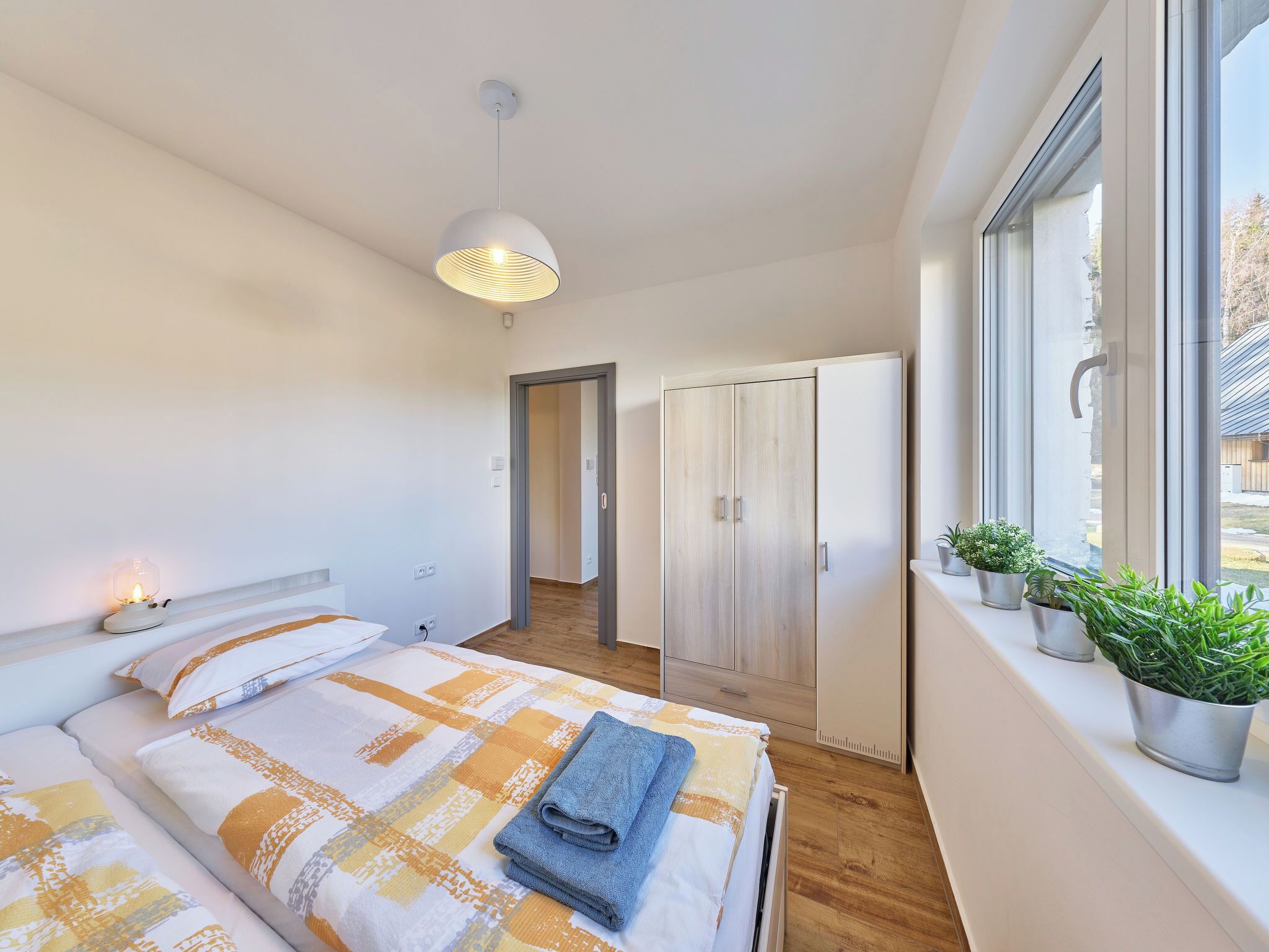 Ein modernes Schlafzimmer mit Bett, Nachttischlampe, Kleiderschrank und einem Fenster mit Pflanzen.