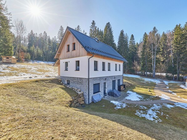 A two-story house with a stone foundation, a sloped roof, and a small attached wooden structure.