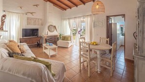 A spacious living area with a high wooden ceiling, a dining table with chairs, a sofa, a television, and a fireplace. - Biniroma by 3 Villas Menorca (Binibéquer Vell)