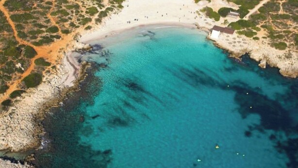 An aerial view of a coastal area with a sandy beach, clear turquoise waters, and rocky terrain. - Biniroma by 3 Villas Menorca (Binibéquer Vell)