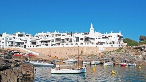 A coastal town with white buildings, a prominent church, and boats anchored near the shore. - Biniroma by 3 Villas Menorca (Binibéquer Vell)