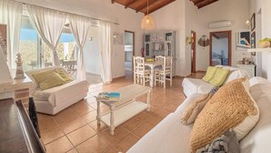 A spacious living area with a high ceiling, a dining table, and a cozy seating arrangement. - Biniroma by 3 Villas Menorca (Binibéquer Vell)