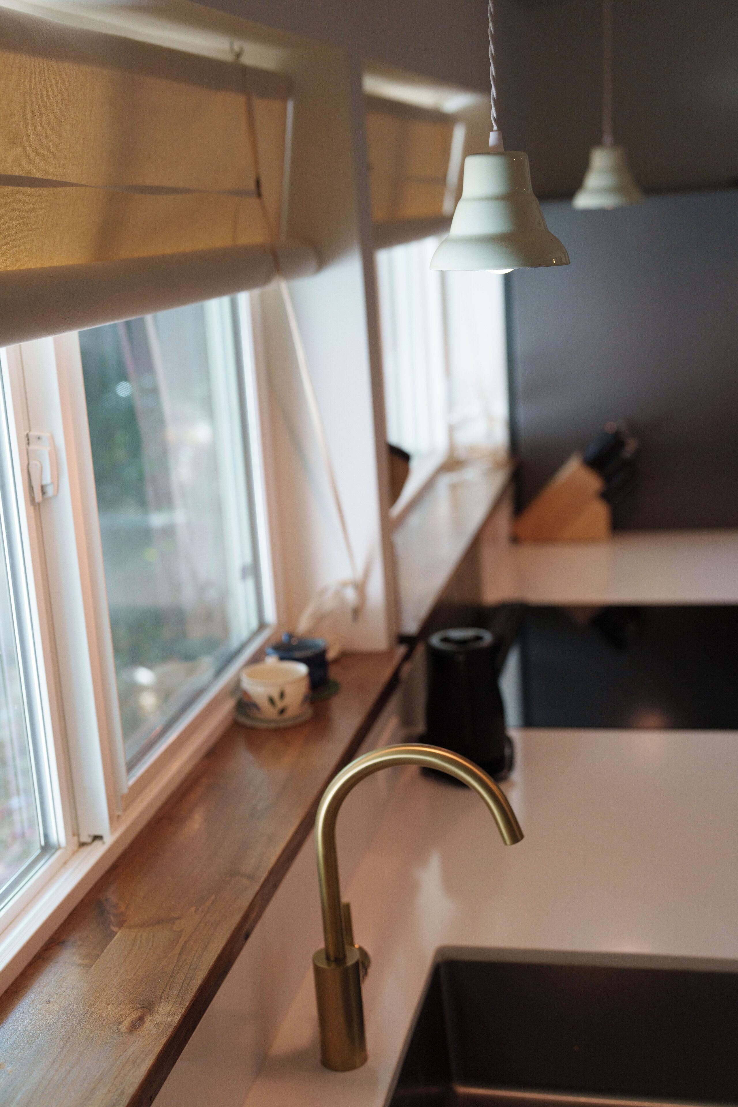 A kitchen with a wooden countertop, a stainless steel sink, and hanging pendant lights.