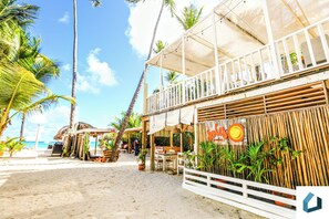 A beachside restaurant with outdoor seating, palm trees, and a view of the ocean. - Lovely Beach-front Complex Fun Pools Dining Shops (Punta Cana)