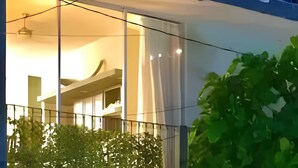 Ein modernes Gebäude mit Balkon, einem geparkten Auto davor und einem Baum im Vordergrund.