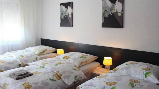 A hotel room with two beds, each with floral-patterned bedding and pillows. There are two wall-mounted lamps on the nightstands. - Studio near Basel Airport RM1142 (Saint-Louis)