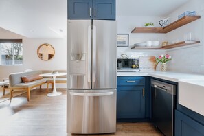 Una cocina moderna con un refrigerador de acero inoxidable, armarios azules y un comedor con mesa blanca y sofá.
