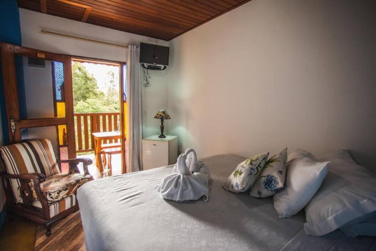 A bedroom with a bed, pillows, a chair, a nightstand, a lamp, and a TV.