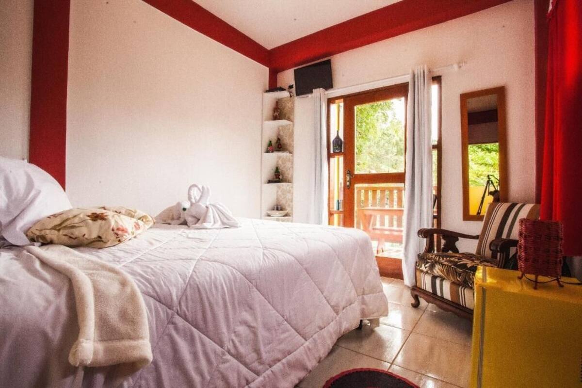 A bedroom with a bed, a wooden chair, a small table, and a door leading to a balcony.