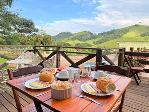 A wooden table set outdoors with plates of food, a bowl of pastries, and a glass of water. - Pousada Refúgio dos Palmares (São Bento do Sapucaí)