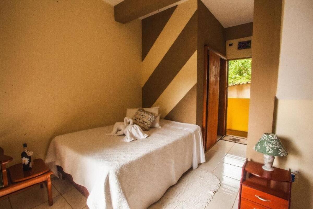 A bedroom with a bed, bedside table, lamp, and a view of the outside.