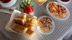 A round table with various dishes and drinks, including salads, meats, and bread, set on a patterned tablecloth. - Guest house River side  (Mestia)