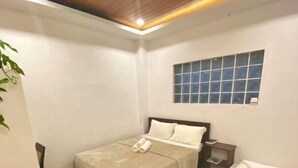 A small, well-lit room with two beds, wooden flooring, a window, and a ceiling with recessed lighting. - Cozy Stay at Jezette’s Inn (Barangay 5, Sipalay City)