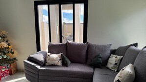 A grey sectional sofa with multiple cushions, a small Christmas tree, and a window with blinds. - Villa Idalia (Comayagua)