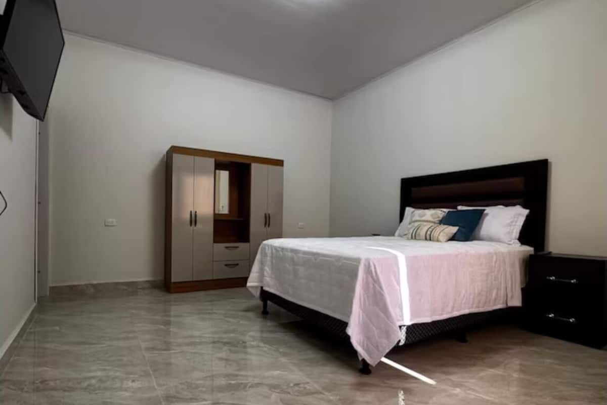 Un dormitorio con cama, armario, mesita de noche y televisor de pantalla plana montado en la pared.