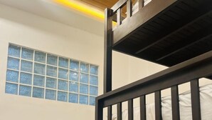 A bunk bed with a mattress and pillows, a window with blue-tinted glass, and a wooden floor. - Jezette’s Inn | Peaceful, Cozy Stay (Sipalay City)