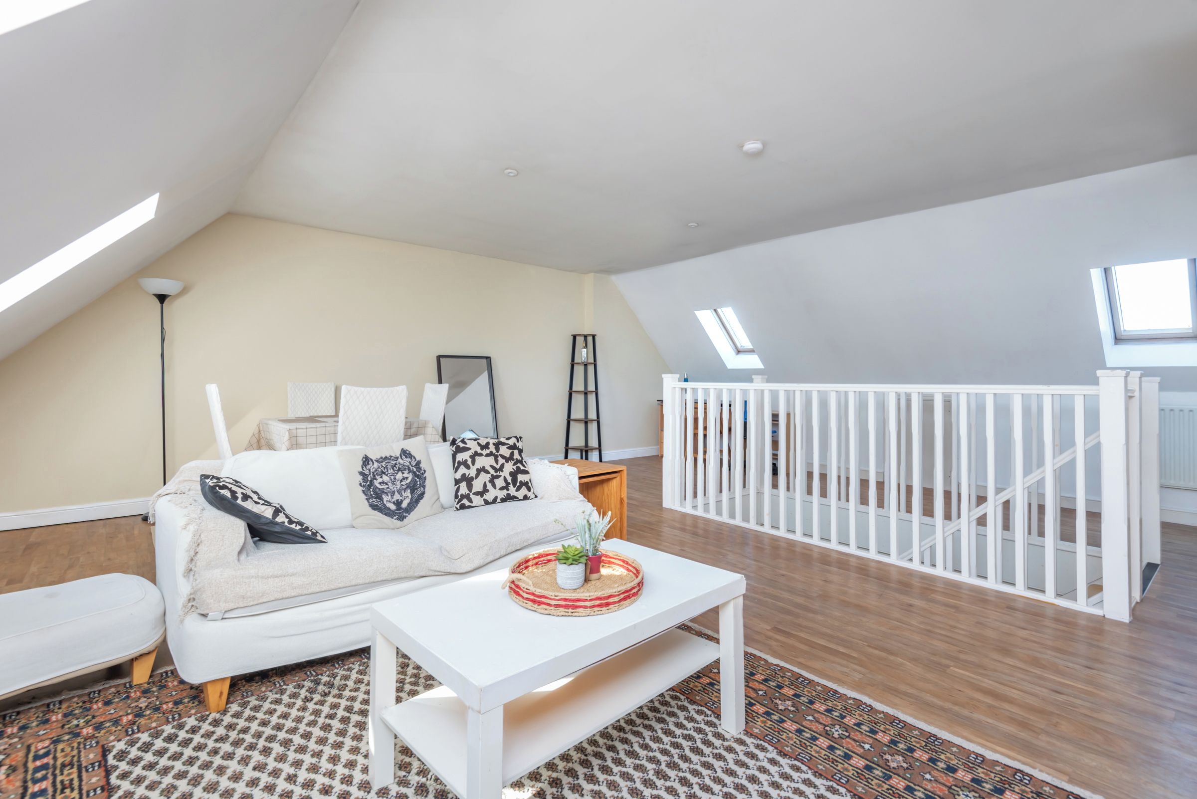 A spacious loft with a high ceiling, a white sofa with patterned cushions, a small white coffee table, and a patterned rug.
