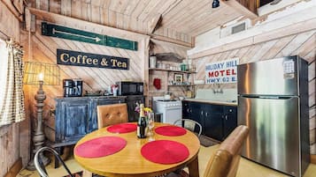 A rustic kitchen with a coffee and tea sign, a refrigerator, and a table with red placemats.