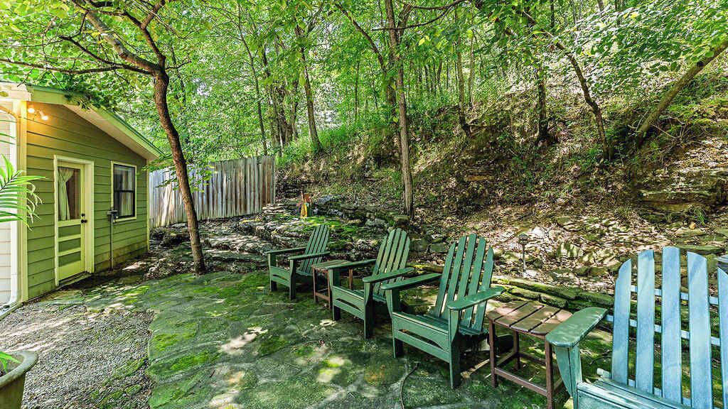 A rustic outdoor seating area with Adirondack chairs and a small table, surrounded by a wooden fence and lush greenery.