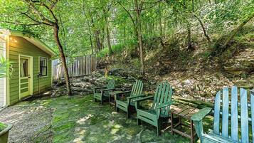 A rustic outdoor seating area with Adirondack chairs and a small table, surrounded by a wooden fence and lush greenery.