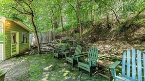 Un espace extérieur aménagé dans un style rustique, avec des fauteuils Adirondack et une petite table, le tout entouré d’une clôture en bois et d’une végétation luxuriante.