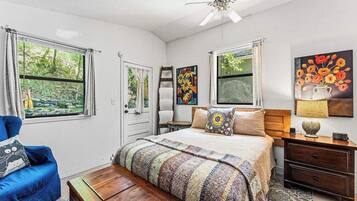 A bedroom with a bed, a chair, a nightstand, a dresser, and two windows with curtains.