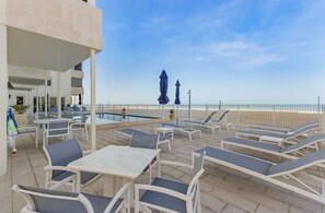 A rooftop pool area with lounge chairs and tables, overlooking a beach. - Beachfront Condo on Bonita Beach  - SeaGlass Shores (Bonita Springs)