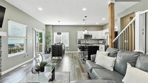 Uma sala de estar moderna com um sofá cinzento, uma mesa de centro de vidro e uma área de jantar com mesa e cadeiras.