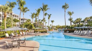 En pool vid ett semesterhotell med solstolar, palmer och en klarblå himmel.