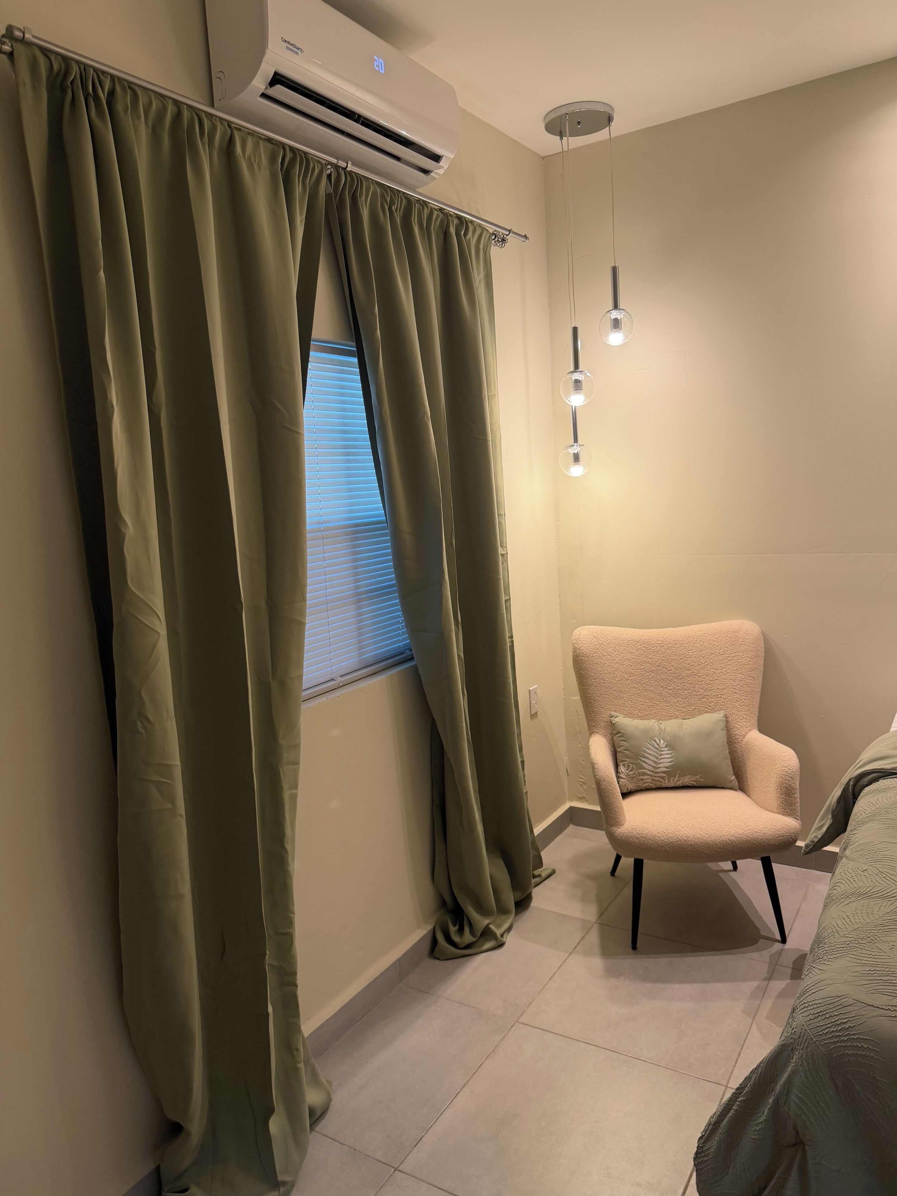 Una habitación con ventana, aire acondicionado, una silla y una lámpara colgante.