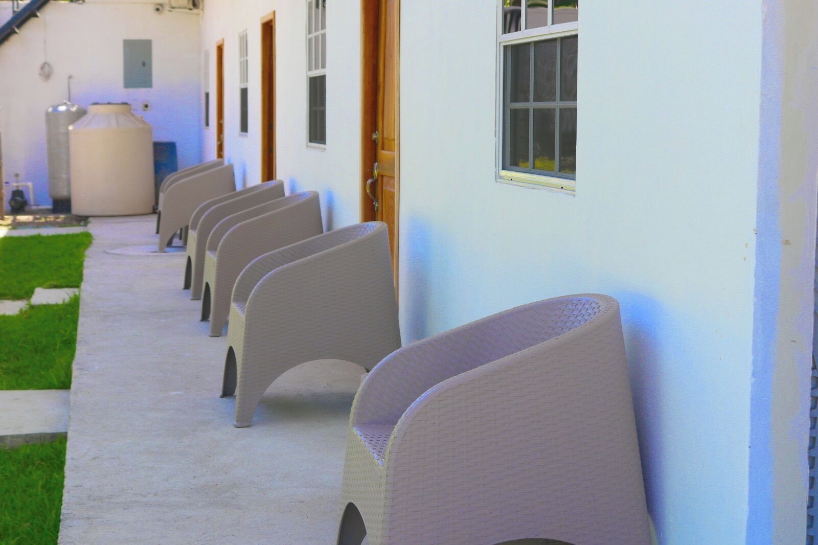 A row of chairs against a building wall, a large water tank, and a grassy area.