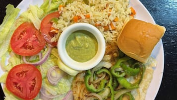A plate with rice, vegetables, a piece of meat, a bun, and a small bowl of sauce.