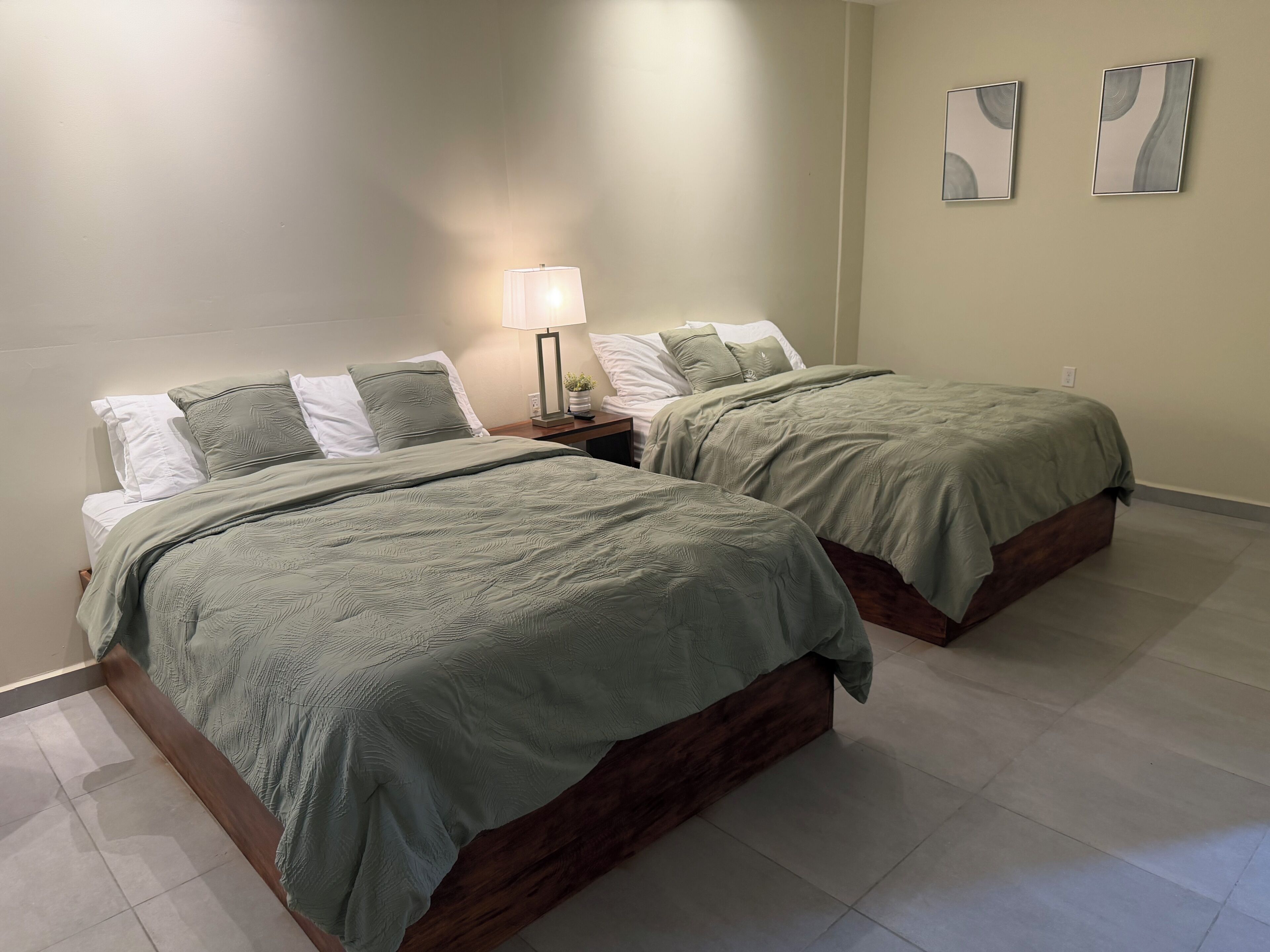A bedroom with two beds, a nightstand, a lamp, and two wall art pieces.
