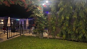 Un espacio exterior bien iluminado con luces colgantes, césped y plantas en macetas.