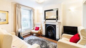A living room with a fireplace, a television, and a comfortable seating area. - Classic Pimlico Townhouse (London)