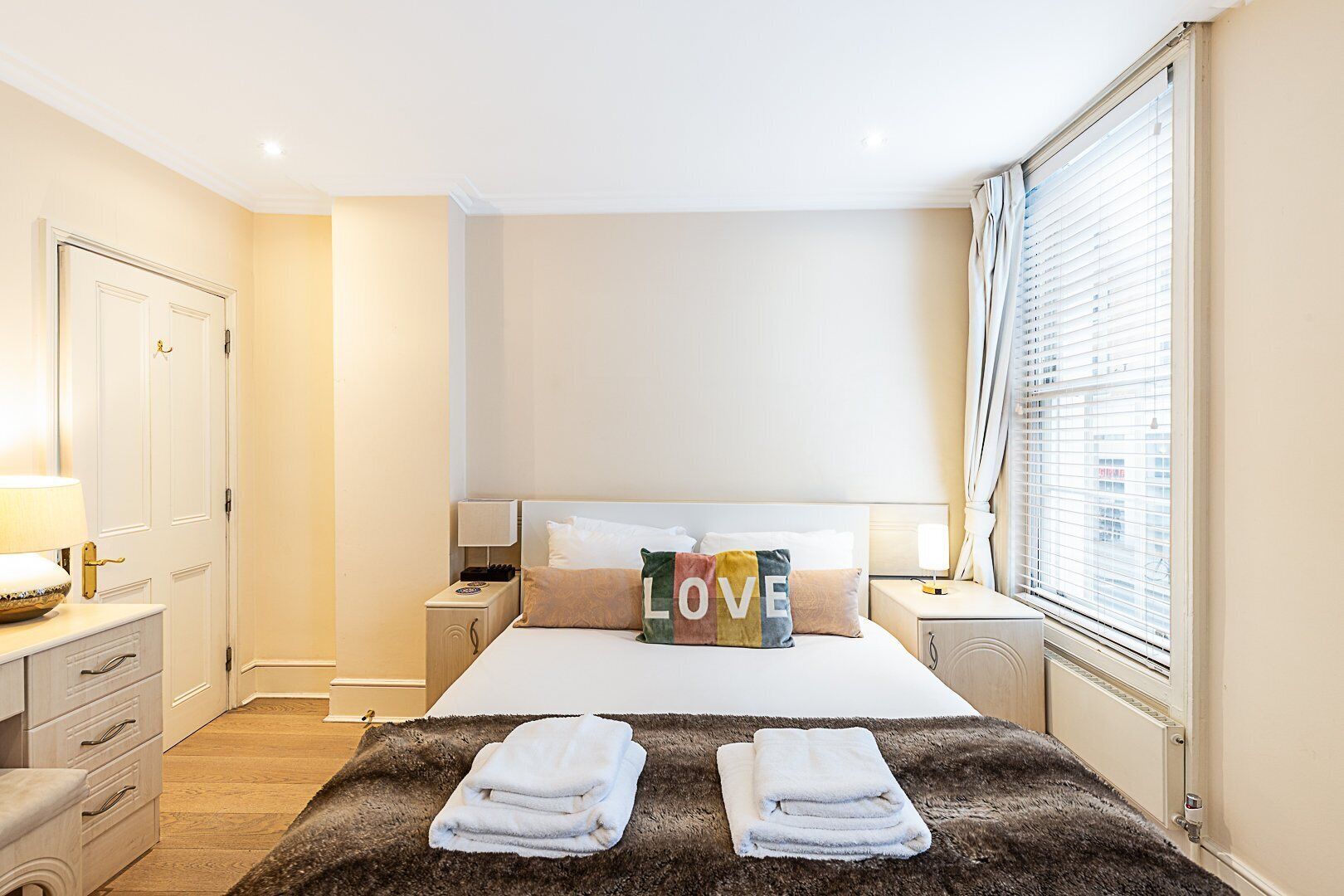 Quarto de hotel com cama, duas mesas de cabeceira, um guarda-roupa e janela com persianas.