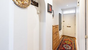 A hallway with a patterned rug, wooden dresser, and wall-mounted artwork. - Classic Pimlico Townhouse (London)