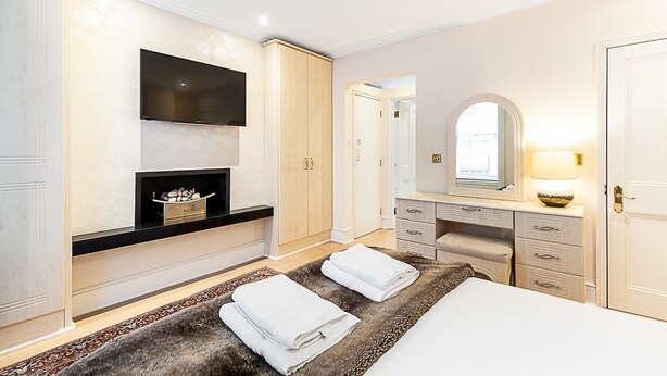 A modern bedroom with a large bed, a vanity with a mirror, a fireplace, and a walk-in closet. - Classic Pimlico Townhouse (London)